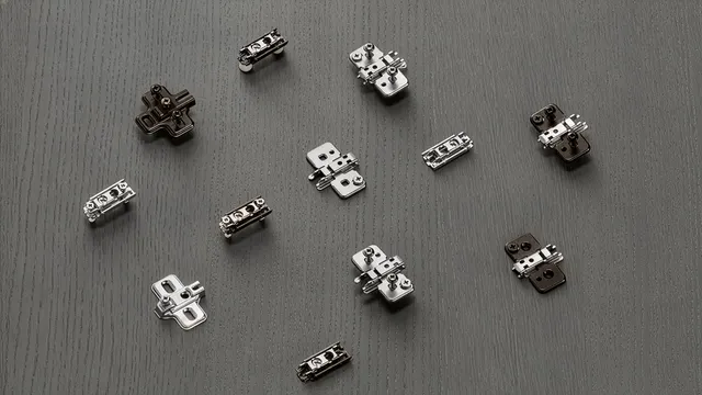 Verschiedene Blum-Montageplatten in Kreuz- und Linearform, Nickel und Onyx black, auf dunkler Holzfläche