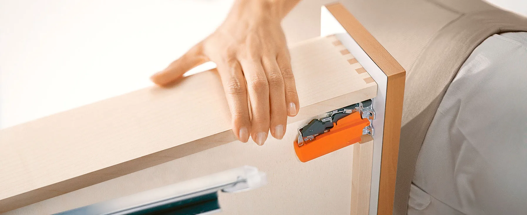 Blum Kupplung im eingebauten Zustand unter einem Holzschubkasten, sichtbar als oranger Rast-Bügel der TANDEM-Variante