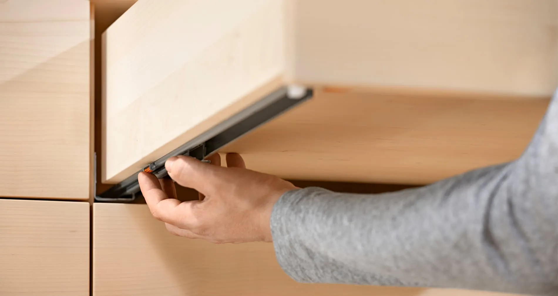 Hand am orangenen Stellrad zur Tiefeneinstellung an der Blum TANDEM TIP-ON-Schiene