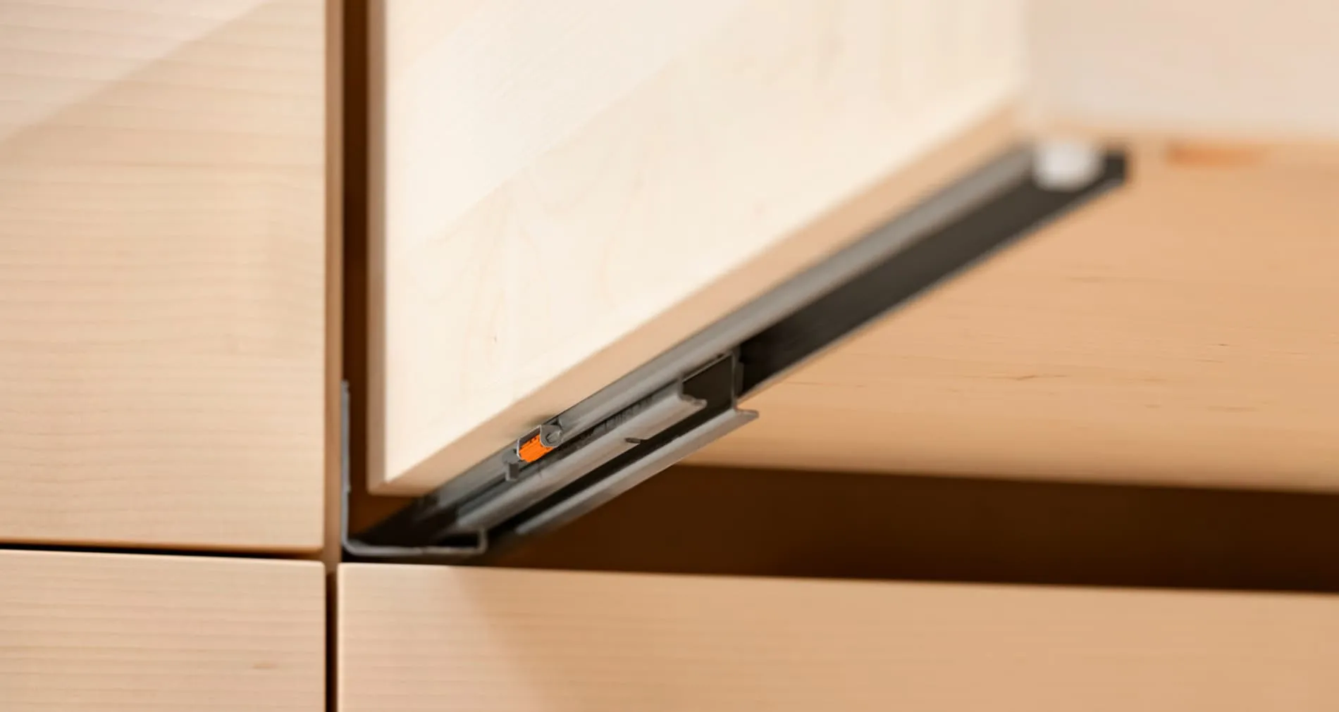 Eingebaute Blum TANDEM TIP-ON-Schiene am Holzschubkasten mit sichtbarem orangenen Hebel für die Tiefeneinstellung